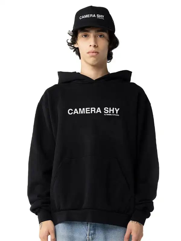 Front View Of oversized black pullover hoodie with the white text 'CAMERA SHY'.