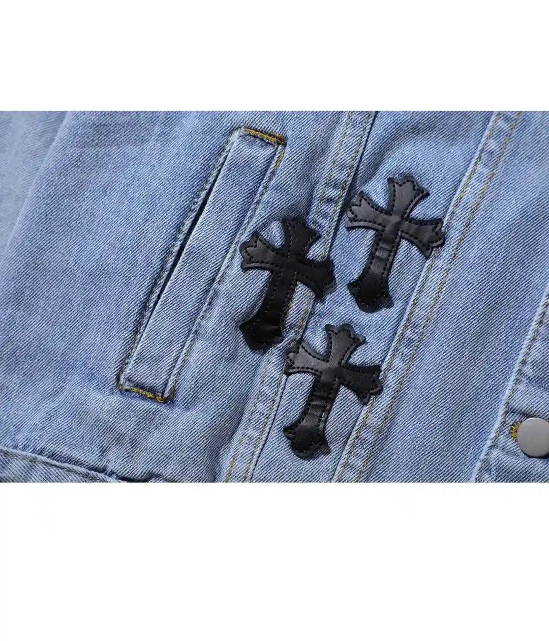 Close-up view of a light blue denim jacket highlighting black cross patches near the chest pocket.
