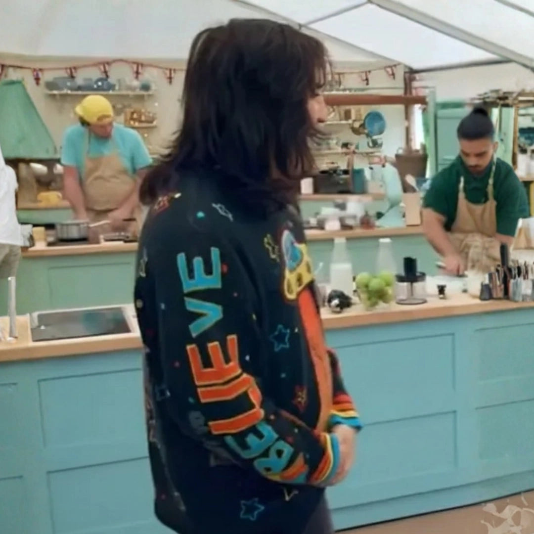Person wearing a colorful jacket with 'BELIEVE' text in a kitchen setting