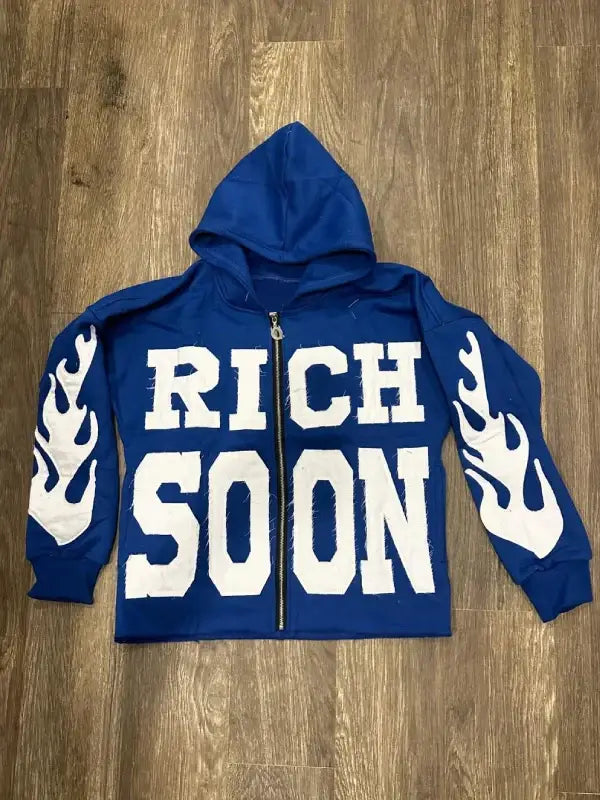 Front view of blue zip-up hoodie featuring 'RICH SOON' text