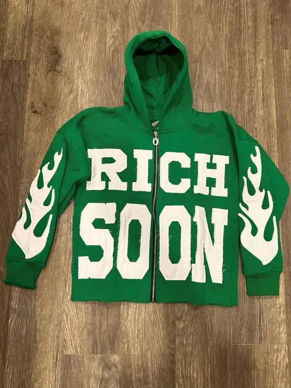 Front view of green zip-up hoodie featuring 'RICH SOON' text