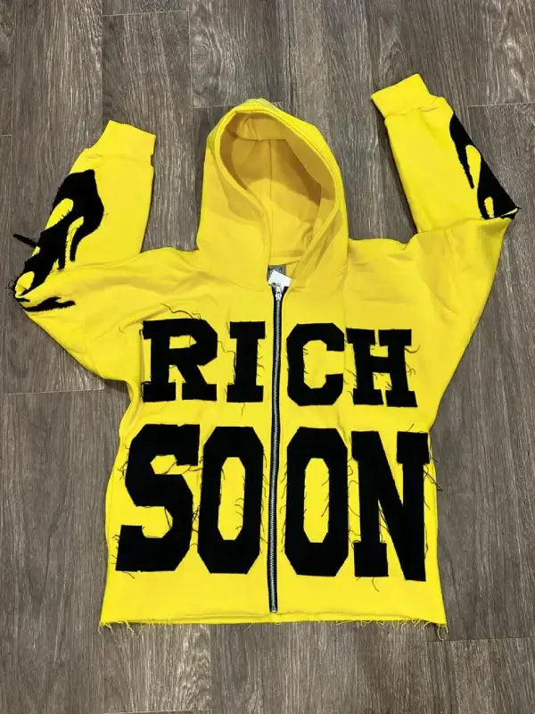 Front view of yellow zip-up hoodie, featuring 'RICH SOON' text