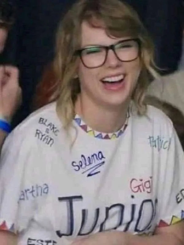 Taylor Swiftwearing a Junior Jewels Shirt with various names printed on it, laughing.
